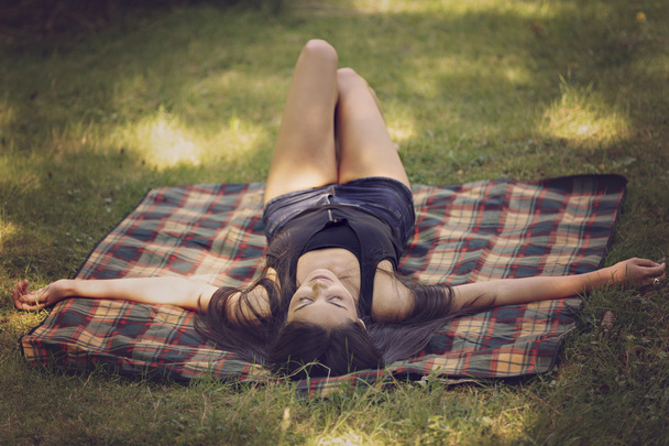 όμορφη νεαρή γυναίκα βρίσκεται σε μια κουβέρτα και να χαλαρώσετε στη φύση - Φωτογραφία, εικόνα