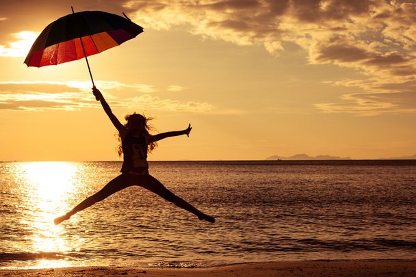 Happy girl with an umbrella jumping on the beach - Valokuva, kuva