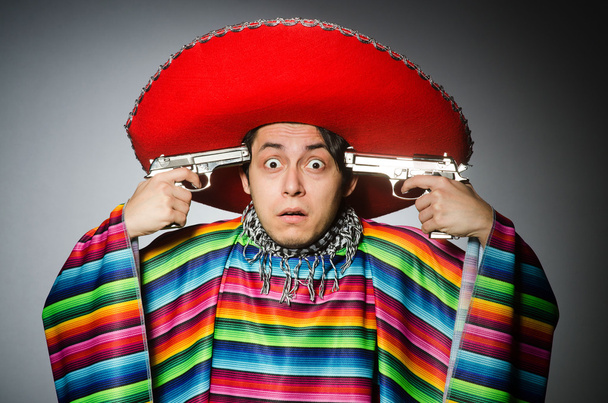 Человек в ярком мексиканском пончо держит пистолет против серого - Фото, изображение