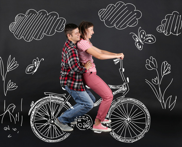 Funny young couple ride the bike, on black background - Foto, Imagem