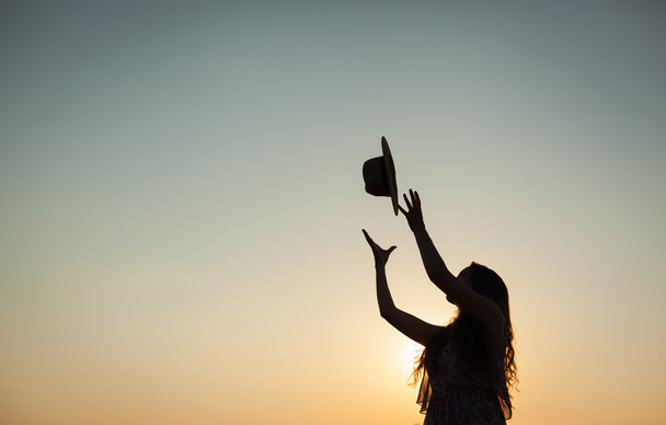 Woman throwing hat at sunset - Photo, Image