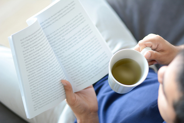 Un uomo che legge libro con tazza di tè caldo in un'altra mano
 - Foto, immagini