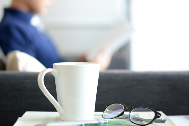 Φλιτζάνι καφέ, γυαλιά & στυλό πάνω από ένα βιβλίο με φόντο θαμπάδα ενός βιβλίου ανάγνωση άνθρωπος - Φωτογραφία, εικόνα