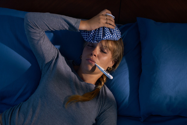 Dívka s horečkou drží teploměr v ústech v noci - Fotografie, Obrázek