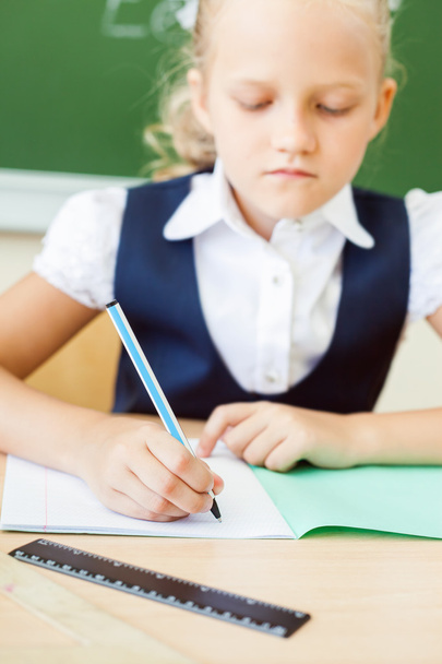 schoolgirl sitting at desk at school and writing to notebook - Foto, Imagen