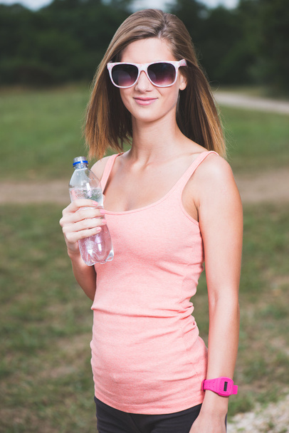 Menina fitness sedenta segurando garrafa de água
 - Foto, Imagem