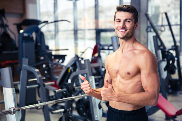 Muscular man showing thumbs up at gym - Foto, imagen