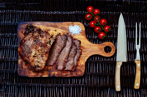 Op de tafel is een houten plank waarop de chef-kok een stuk vlees in porties gesneden - Foto, afbeelding