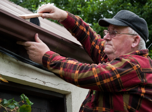старший мужчина чистит водосток снаружи дома
 - Фото, изображение
