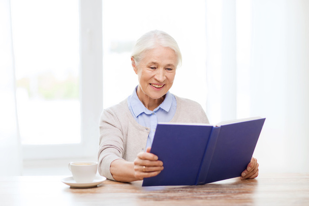 щаслива усміхнена старша жінка читає книгу вдома
 - Фото, зображення