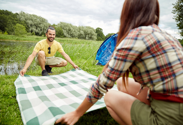 happy couple laying picnic blanket at campsite - Fotografia, imagem