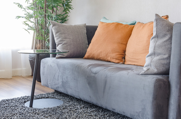 modernes graues Sofa mit orangefarbenen Kissen und rundem schwarzem Tisch - Foto, Bild