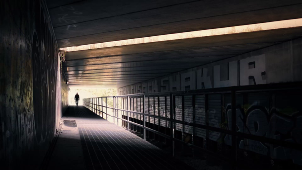 Hombre camina bajo puente en iluminación dramática
 - Metraje, vídeo
