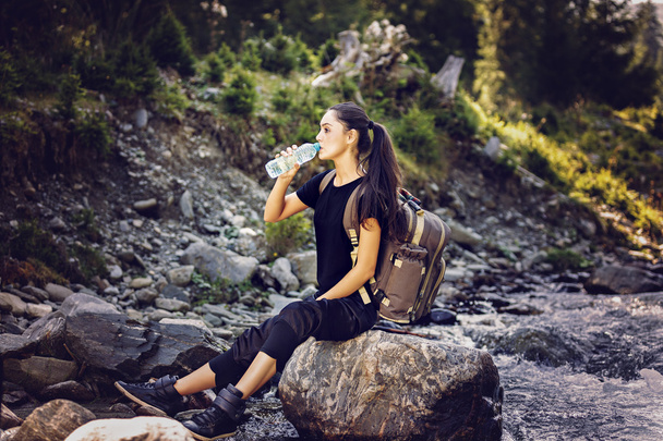 hermosa mujer descansando sobre una roca en el río y bebiendo wate
 - Foto, Imagen