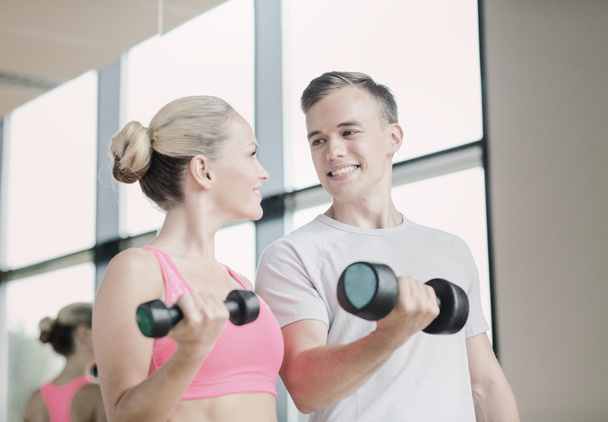 smiling young woman with personal trainer in gym - Valokuva, kuva