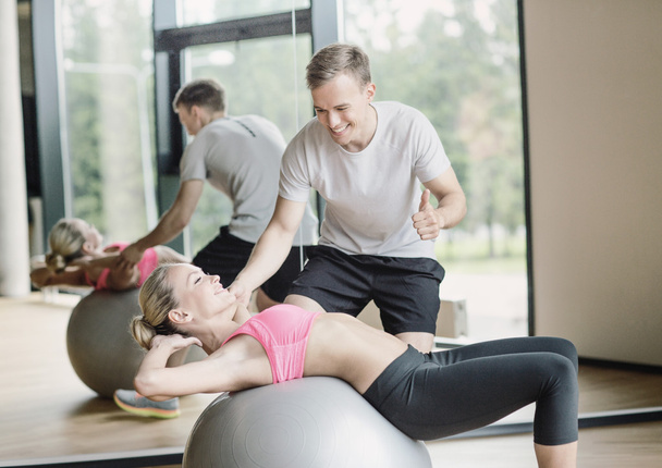 smiling young woman with personal trainer in gym - Foto, Imagen