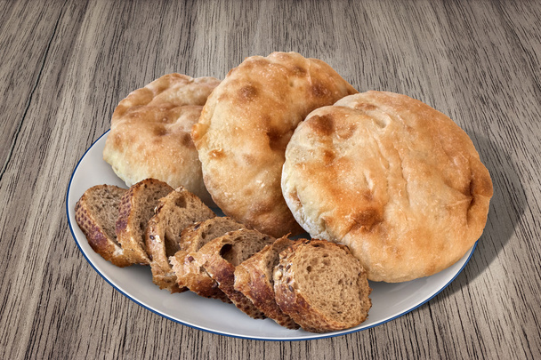 Piatto di fette integrali di pane baguette con fette di pane pita su tavola di legno
 - Foto, immagini
