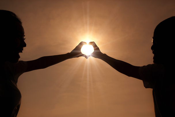 Happy young couple making heart shape with hands at sunset - Photo, image