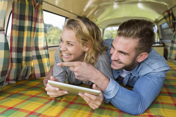 young couple with vintage camper van using touchpad - Foto, afbeelding