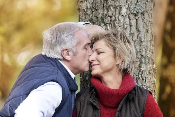 Pareja de mediana edad besándose por árbol
 - Foto, Imagen