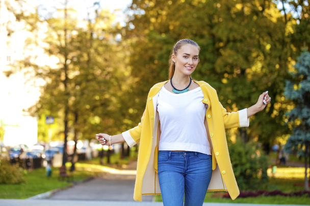 Happy young woman in yellow coat in autumn street - Foto, Imagen