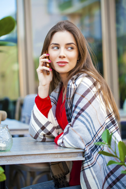Young beautiful girl sits in summer cafe and calling by phone - Foto, Imagen