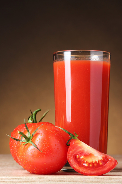 Tomato juice in glass and tomato on wooden table on brown backgr - 写真・画像