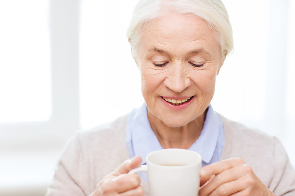 happy senior woman with cup of tea or coffee - 写真・画像
