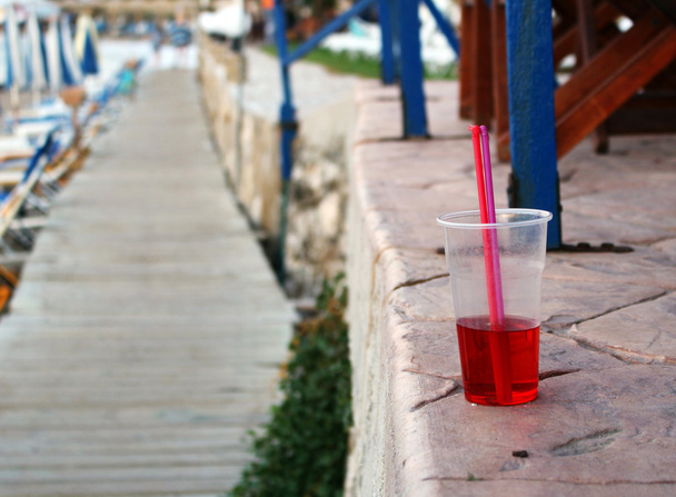Холодный красный напиток с соломинкой на пляже
 - Фото, изображение