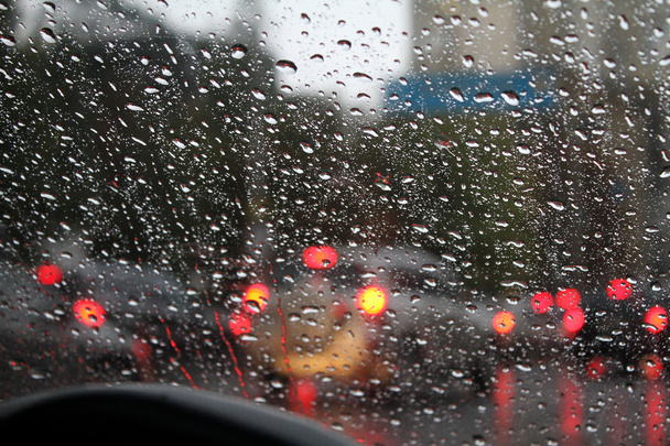 Blick auf die Wassertropfen auf der Windschutzscheibe des Autos bei Regen auf der Stadtstraße - Foto, Bild