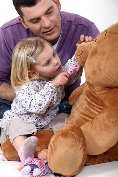 Father and daughter playing dentist with a teddy bear - 写真・画像