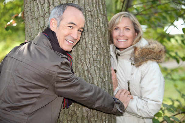 Older couple hugging a tree trunk in the autumn - Photo, Image