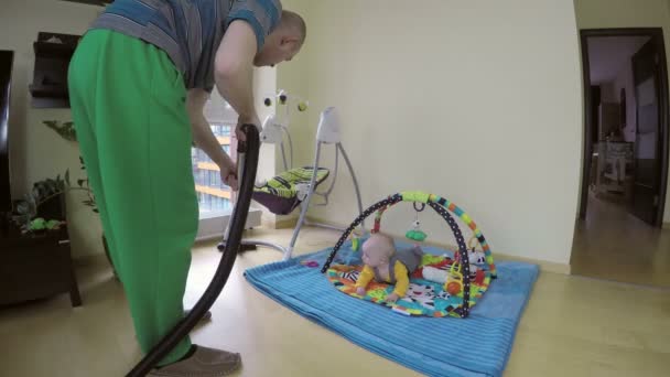 hombre piso de limpieza con aspiradora y bebé curioso en la alfombra de juego. 4K
 - Imágenes, Vídeo