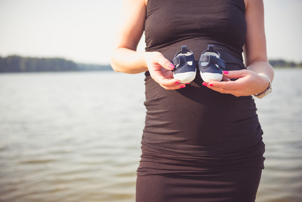 Beautiful pregnant woman holding tiny shoes - Foto, afbeelding