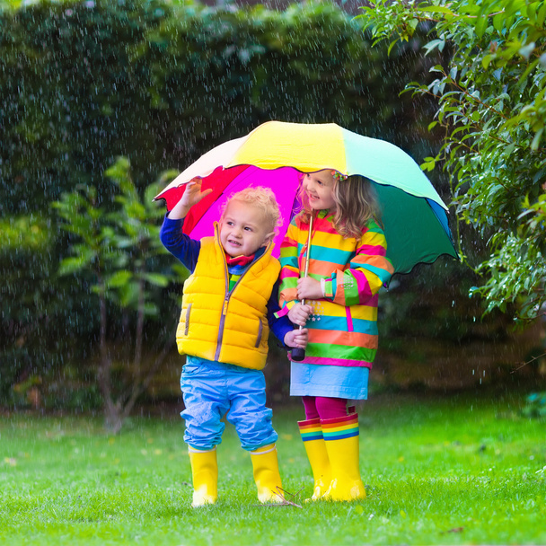 Діти грають під дощем під барвистою парасолькою
 - Фото, зображення