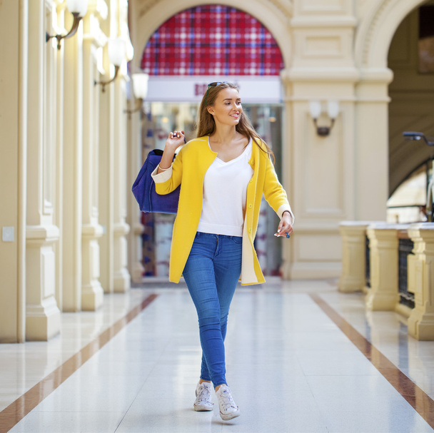 Young woman in yellow coat walking in the shop - Zdjęcie, obraz