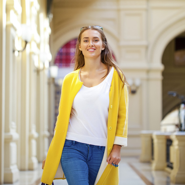 Young woman in yellow coat walking in the shop - Photo, image