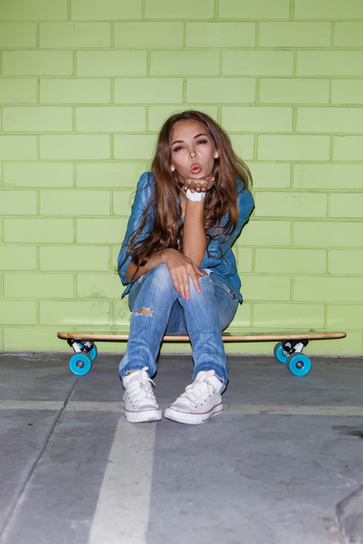 beautiful long-haired girl with a wooden skateboard near a green - Foto, imagen