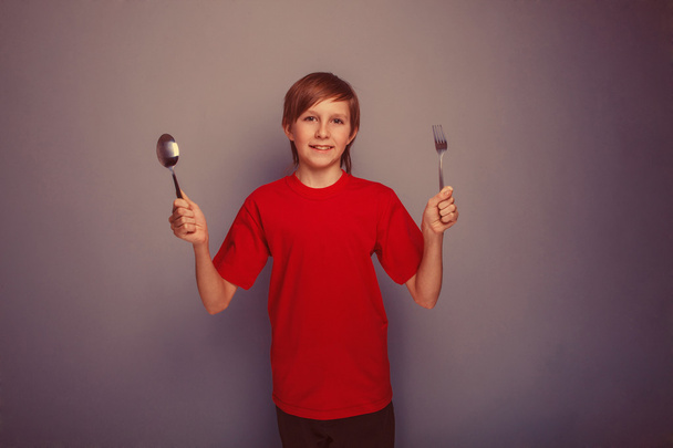 Έφηβο αγόρι δώδεκα χρόνια σε ένα κόκκινο πουκάμισο κρατώντας ένα κουτάλι και για - Φωτογραφία, εικόνα