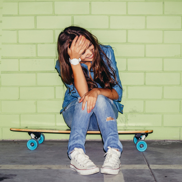beautiful long-haired lady with a wooden skateboard near a green - Fotografie, Obrázek