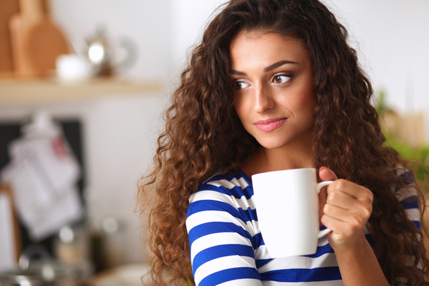 A young woman with a cup of tea in her kitchen - Foto, Imagen