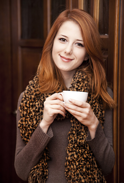 Tyyli punapää tyttö juo kahvia lähellä puu ovet
. - Valokuva, kuva