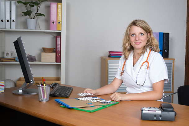 Привлекательная блондинка-доктор с таблетками на столе
 - Фото, изображение