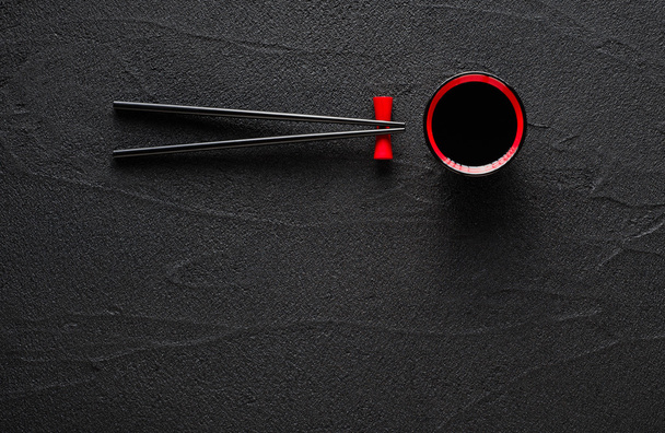 Chopsticks and bowl with soy sauce on black stone background - Photo, Image