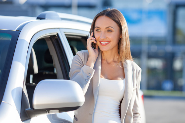 Attractive young woman is using telephone near vehicle - Foto, Imagem