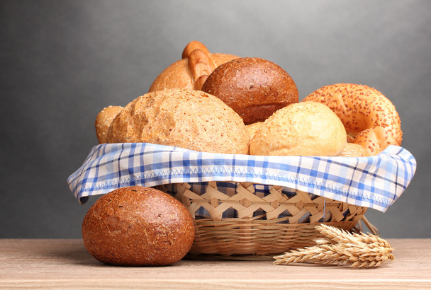 Delicious bread in basket and ears on wooden table on gray background - Fotografie, Obrázek