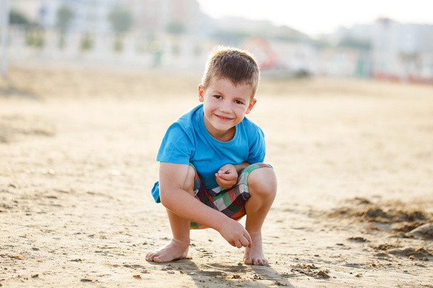 Kis fiú zömök-homok a strandon - Fotó, kép