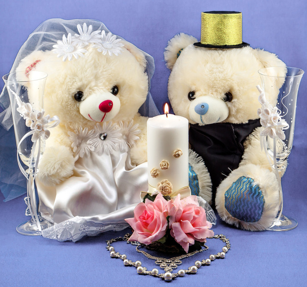 Wedding setting: hand made boy and girl teddies, white and gold candle, wedding glasses and pearl silver necklace in form of heart on textured blue background - Photo, Image