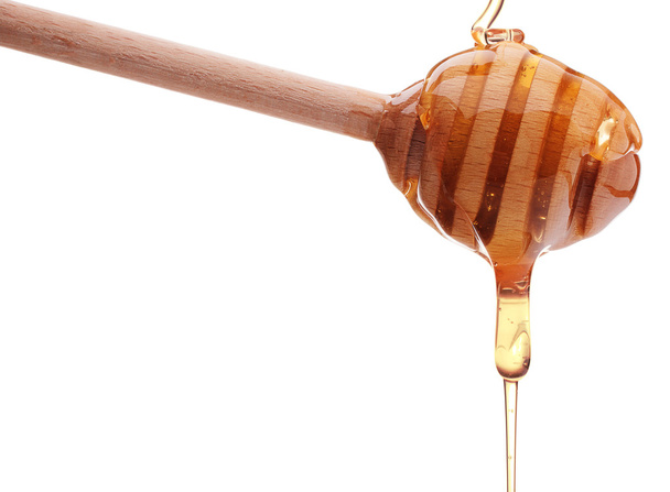 Honey dripping from wooden honey dipper - Foto, afbeelding