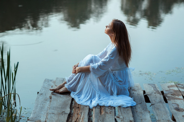 Meisje, zittend op een houten pier en dromen. - Foto, afbeelding